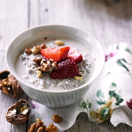 Chia pudding in a bowl with a spoon and strawberries on the side